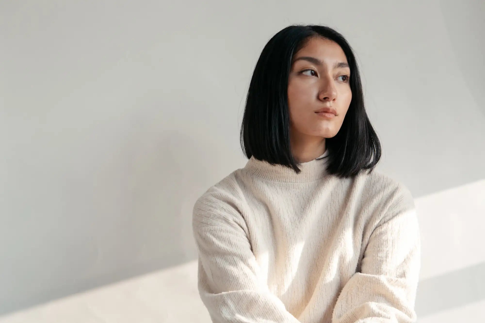 Eine Frau trägt einen weichen, offweiß gestrickten Pullover mit Rippenstruktur und hohem Ausschnitt.